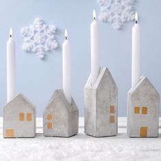 five candles are lined up in front of small houses and snowflakes on the wall