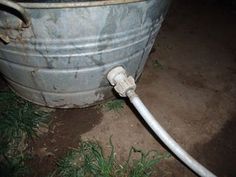 a white hose connected to a large metal barrel with grass growing around it and dirt on the ground