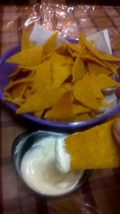 someone is dipping tortilla chips into a bowl with sour cream on the side