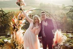 a man and woman standing next to each other in front of an arch with flowers