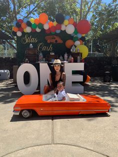 a woman sitting on top of an orange car in front of a sign that says one