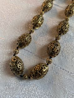 Vintage Monet gold tone filigree bead necklace  Quality piece, heavy and substantial  It measures 24 inches long inc the extender chain  In excellent condition, beads are knotted onto cord Oval beads approx 20 mm x 13 mm in size Gold Filigree Costume Jewelry Necklace, Gold Filigree Necklaces For Parties, Bronze Filigree Metal Necklace, Bronze Metal Necklace With Filigree, Bronze Metal Filigree Necklace, Gold Beaded Necklaces With Spacer Beads For Formal Occasions, Elegant Gold Beaded Necklace With Large Beads, Vintage Gold Jewelry With Polished Beads, Antique Gold Metal Necklace With Filigree