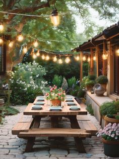 a wooden picnic table sitting in the middle of a garden with lights strung over it