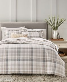 a bed with plaid comforter and pillows in a white room next to a night stand