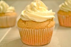 two cupcakes with white frosting sitting on a table next to a teacup