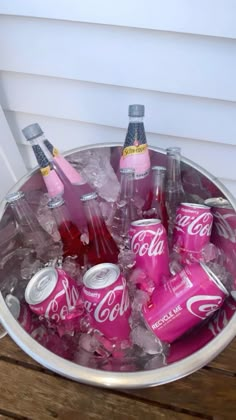 a bucket filled with pink sodas sitting on top of a wooden table