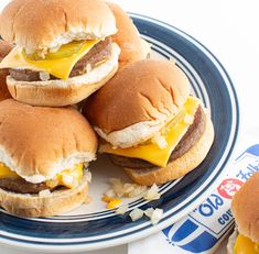 hamburgers with cheese and onions on a plate next to a bottle of pepsi soda