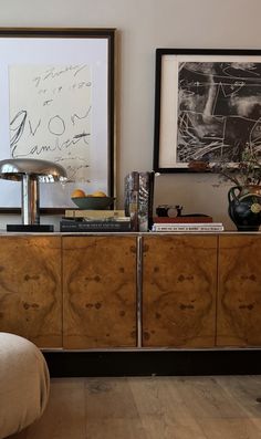 a sideboard with some books on top of it and pictures hanging above the drawers