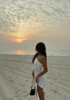 a woman standing on top of a sandy beach next to the ocean in white dress