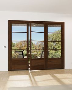 an empty room with two double doors and some windows on the wall, looking out onto a garden