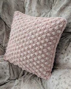 a pink crocheted pillow sitting on top of a bed next to a blanket