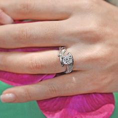 a woman's hand with a diamond ring on her finger and a pink flower in the background