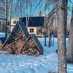 a pile of wood sitting in the snow next to some trees and a building with windows