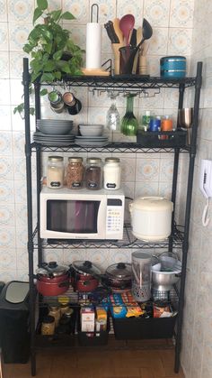 a kitchen shelf filled with pots and pans next to a wall mounted microwave oven