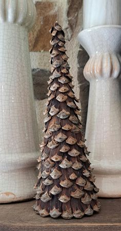 two white vases with pine cones on top of them and one in the foreground