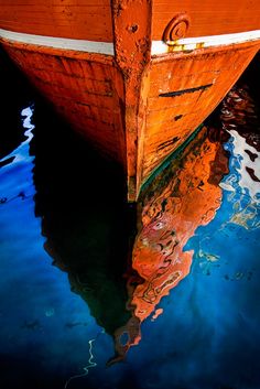 an orange boat floating on top of water with its reflection in it's surface