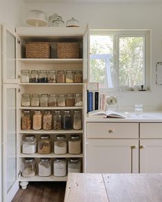 an open pantry with lots of jars and containers on the shelves next to a window