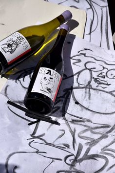 two wine bottles sitting on top of a piece of paper with graffiti written on it