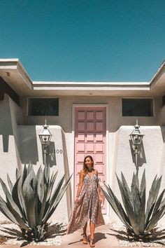 a woman standing in front of a pink door and some cactus plants on the sidewalk