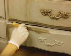 a person in white gloves painting a dresser