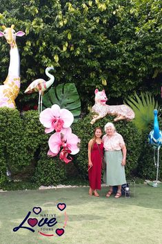 two women standing next to each other in front of some fake animals and flowers on display