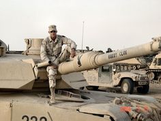 a man sitting on top of a tank next to other tanks in the desert,