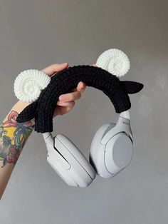 a person holding up two headphones with ears attached to each other, both wearing black and white ear muffs