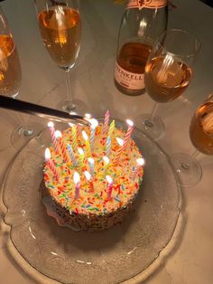 a birthday cake sitting on top of a glass plate next to wine glasses and bottles