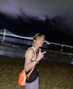 a young man standing on top of a sandy beach next to the ocean with a bridge in the background