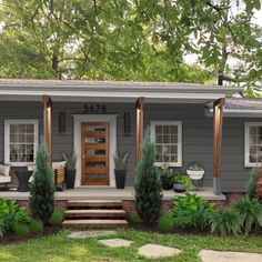 a small gray house with front porch and steps leading up to the door, surrounded by greenery