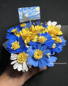 a hand holding a bouquet of blue and yellow flowers with a card in the middle