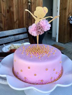 a pink cake with gold sprinkles and a fairy on top