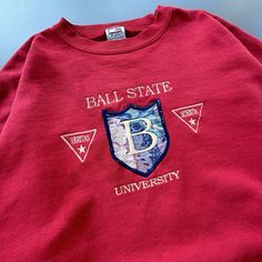 Show off your team spirit with this vintage Ball State University sweatshirt from Crable Sportswear. Perfect for football season, this officially licensed unisex adult sweatshirt is a must-have for any fan of the Ball State Cardinals. The red color and XL size make it a standout piece of fan apparel. Crafted in the USA in the 90s, this crewneck sweatshirt is made to last and has become a beloved souvenir for alumni and fans alike. Whether you're heading to the game or just running errands, this comfortable and stylish sweatshirt is sure to turn heads. Don't miss out on the opportunity to add this piece of college-NCAA history to your collection. Ball State University, University Sweatshirts, Football Season, Team Spirit, Cardinals, State University, Trucker Cap, Running Errands, Ncaa