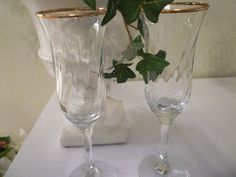 two clear wine glasses sitting on top of a table next to a vase with flowers in it