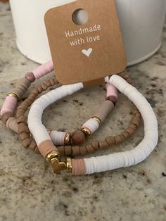 two bracelets with white and pink beads are sitting on the counter next to a cup