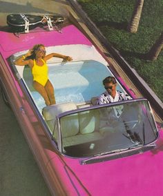 a man and woman riding in the back of a pink car