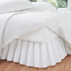 a white bed with pleated bedspread and pillowcases in front of a window