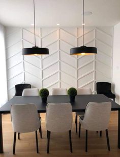 a dining room table with four chairs and two black lamps hanging from it's ceiling