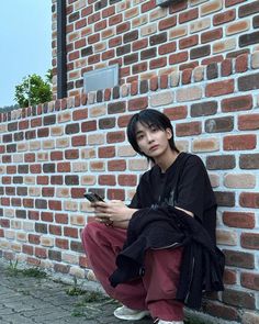 a young man sitting against a brick wall looking at his cell phone