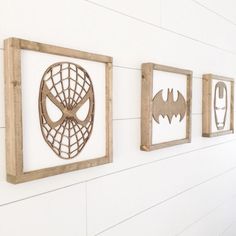 three wooden frames are hanging on the wall with various pictures in them, one has a spiderman mask and two have batman masks