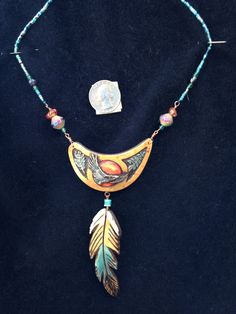 a necklace with beads and a feather on the front is laying on a black surface