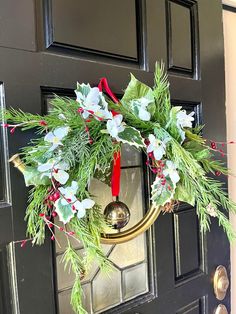 a christmas wreath hanging on the front door with red ribbon and evergreen leaves, white flowers and berries