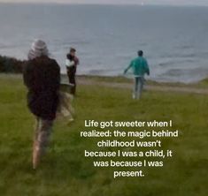 two people are walking in the grass by the water