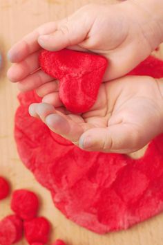 a person holding a heart shaped cookie in their hand next to some red sugar cubes