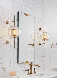 a bathroom with white tile and gold faucet lights on the wall above the sink