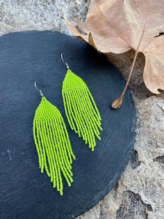 a pair of neon green fringe earrings sitting on top of a stone slab next to a leaf