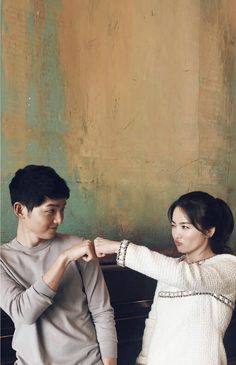 a young man and woman standing next to each other in front of a wooden bench