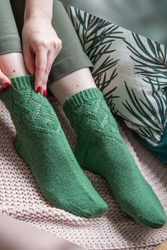 a woman sitting on top of a bed wearing green socks and holding onto her sock