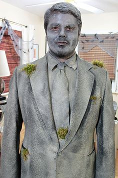 a statue of a man in a suit with moss growing on his lapel coat