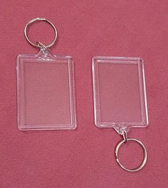 two clear square keychains sitting next to each other on a pink cloth background